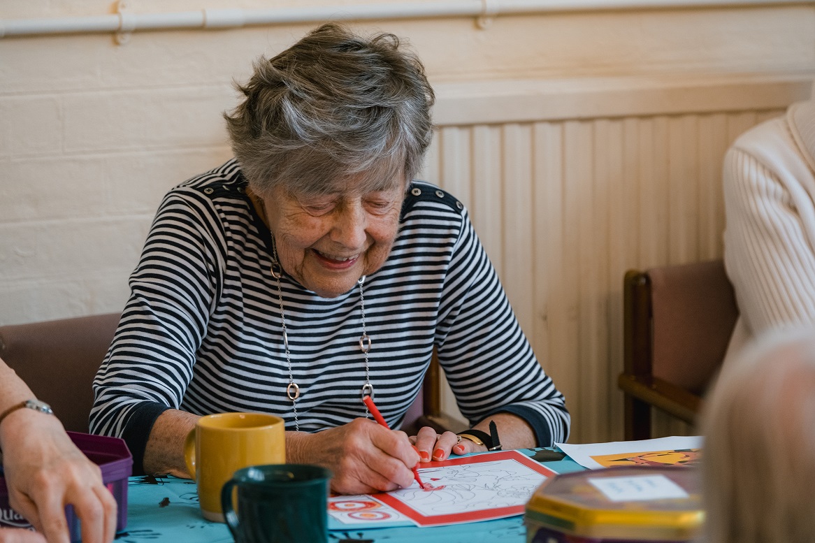 Dementia client smiling with a red pen in her hand whilst doing arts and crafts