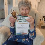 Smiling Wellbeing Client of the Season Award winner holding up her certificate and trophy for her achievements during our Exercise at Home programme.